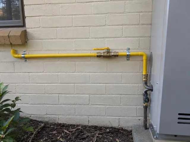 New yellow gas pipe and fittings on an exterior brick wall beside a gas appliance in Baulkham Hills