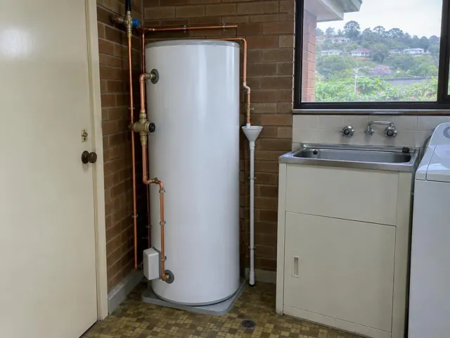 Indoor hot water tank beside a laundry sink and brick wall in Glenhaven